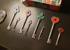 seven antique keys are lined up on a table next to a brooch and pin