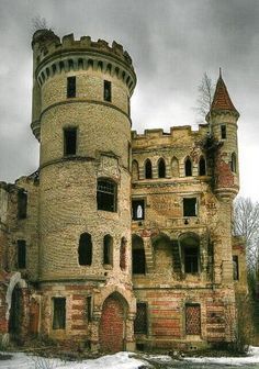 an old abandoned castle with snow on the ground and trees in the foreground, against a cloudy sky