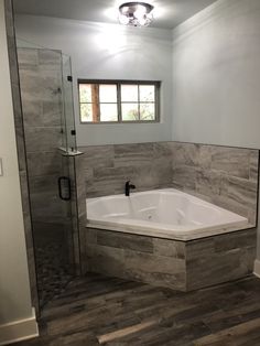 a bathroom with a walk in shower next to a white tub and wooden flooring