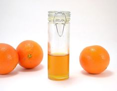 an orange is next to a glass jar with liquid in it and five oranges