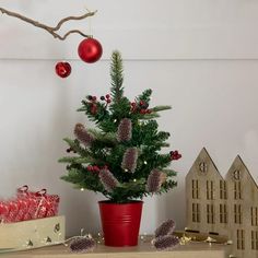 a small christmas tree in a red pot on a table with other decorations and gifts