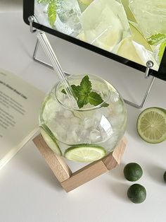 a glass filled with ice and limes next to an open book on a table