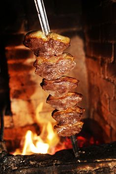 some food is being cooked on a skewer in front of an open fire