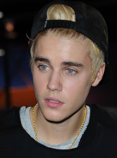 a young man with blonde hair wearing a black hat and gold chain around his neck