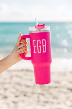 a person holding up a pink coffee cup with the word egb on it in front of an ocean