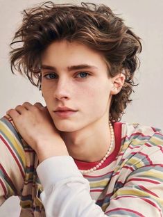 a young man with curly hair wearing a striped shirt and pearls on his necklaces