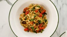 a white bowl filled with pasta and vegetables on top of a marble table next to silverware