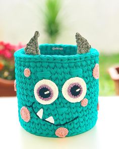 a crocheted monster basket with horns and eyes on it's head, sitting on a table