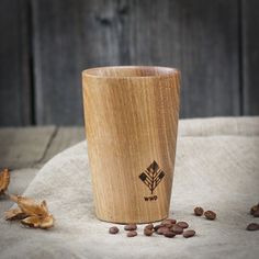 a wooden cup sitting on top of a table next to some coffee beans and leaves