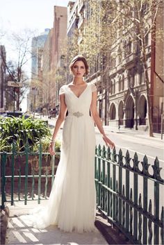 a woman in a white wedding dress standing on a sidewalk next to a green fence