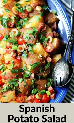 a blue plate topped with potatoes, tomatoes and other vegetables next to a silver spoon