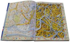 an open book with yellow and blue pins in it's pages, on top of a map