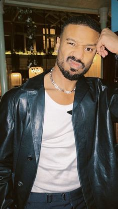 a man in a black leather jacket posing for the camera with his hand on his head