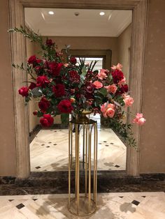 a vase filled with red and pink flowers sitting on top of a marble floor next to a mirror