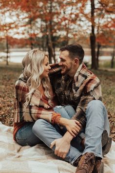 a man and woman sitting on top of a blanket in the woods smiling at each other