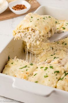 a white casserole dish with chicken and cheese being scooped from the casserole