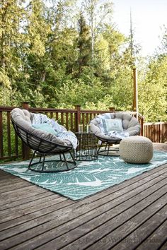 a deck with two chairs and an ottoman on it, in front of some trees