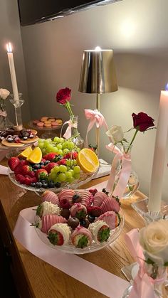 two trays filled with fruit and pastries on top of a wooden table next to candles