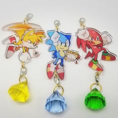 three different colored cartoon keychains on a white surface, one has a sonic the hedgehog charm