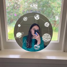 a woman taking a selfie in front of a window with the solar system drawn on it