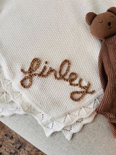 a brown teddy bear laying on top of a white blanket with the word riley written in cursive letters