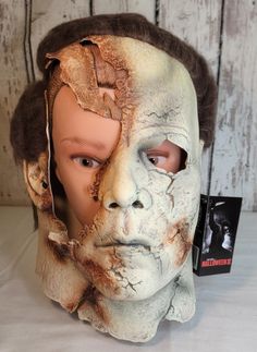 a white mask with brown hair on top of a wooden table next to a book