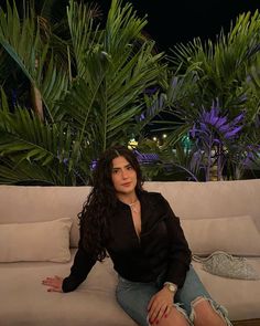 a woman sitting on top of a couch in front of some palm trees at night