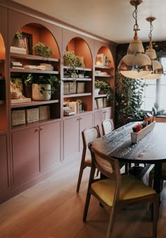 a dining room table with chairs and shelves filled with plants on the wall behind it