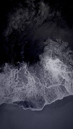 an aerial view of the ocean with waves coming in to shore and dark sky above