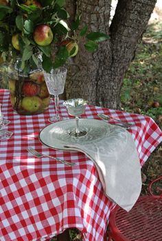 the table is set for two outside with apples in vases and glasses on it