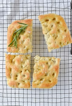 four pieces of bread sitting on top of a cooling rack with rosemary sprigs