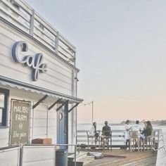 people are standing at the end of a wooden dock near an old building with a cafe sign on it