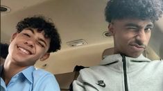 two young men sitting in the back seat of a car, one with curly hair