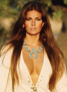 a woman with long brown hair wearing a white shirt and blue necklace on her neck