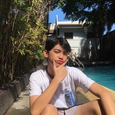 a young man sitting next to a swimming pool