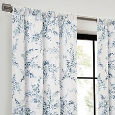 an open window with white curtains and blue flowers on the curtain rod, in front of a large window