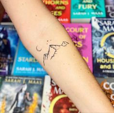 a person's arm with a small tattoo on it and many books in the background