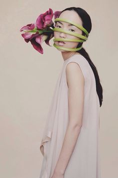 a woman with flowers taped to her face and behind her head is a pink flower