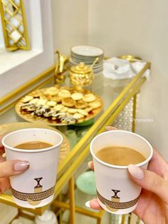 two people holding up coffee cups in front of a table with pastries on it