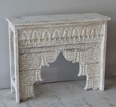 an old white wooden table with carvings on the top and bottom, sitting against a wall