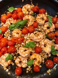 shrimp, tomatoes and corn in a skillet with basil leaves on the side for garnish