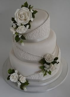 a three tiered wedding cake with white roses on top and green leaves around the edges