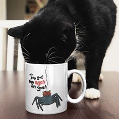 a black and white cat drinking out of a coffee cup on top of a wooden table