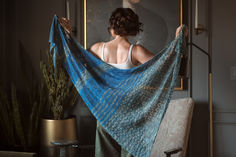 a woman holding up a blue shawl in front of a mirror and potted plant