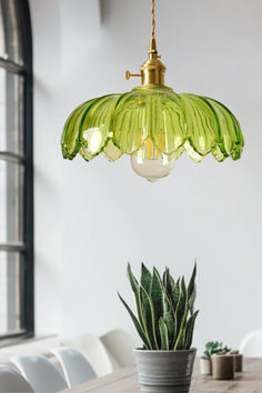 a green glass light hanging over a wooden table next to a potted succulent