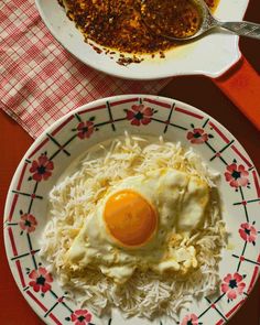 an egg is sitting on top of rice in a bowl next to a plate of food