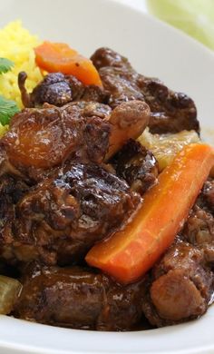 a white plate topped with meat and veggies next to rice on top of a table