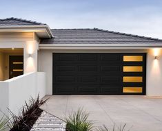 a white house with a black garage door and lights on it's side walk