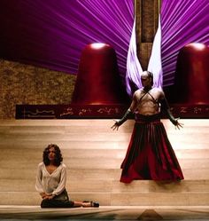 two people sitting on the floor in front of a large purple object with wings above them