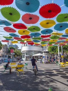 many colorful umbrellas hanging from the ceiling in an open area with tables and chairs